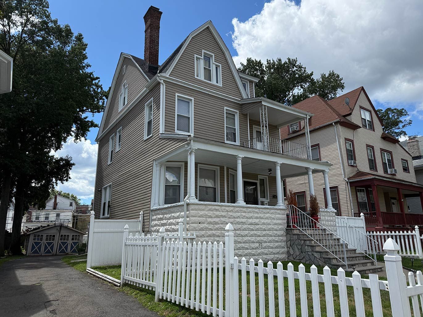 Victorian-style house with gray siding, white trim, and a white picket fence on a residential street