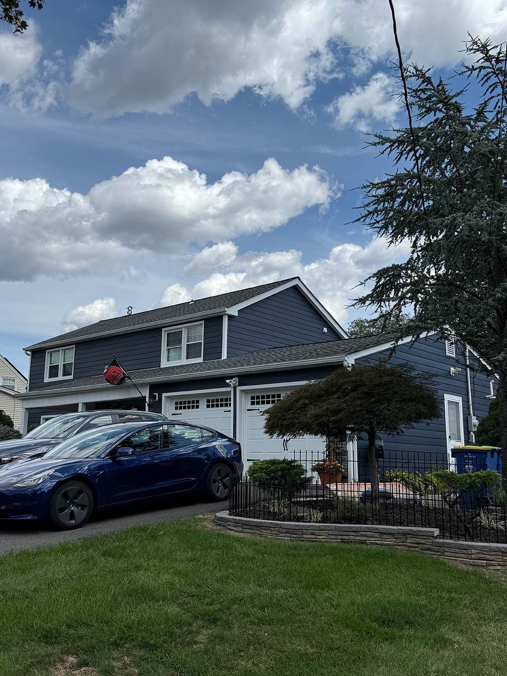 Suburban house with a blue car in the driveway, lawn, and cloudy sky