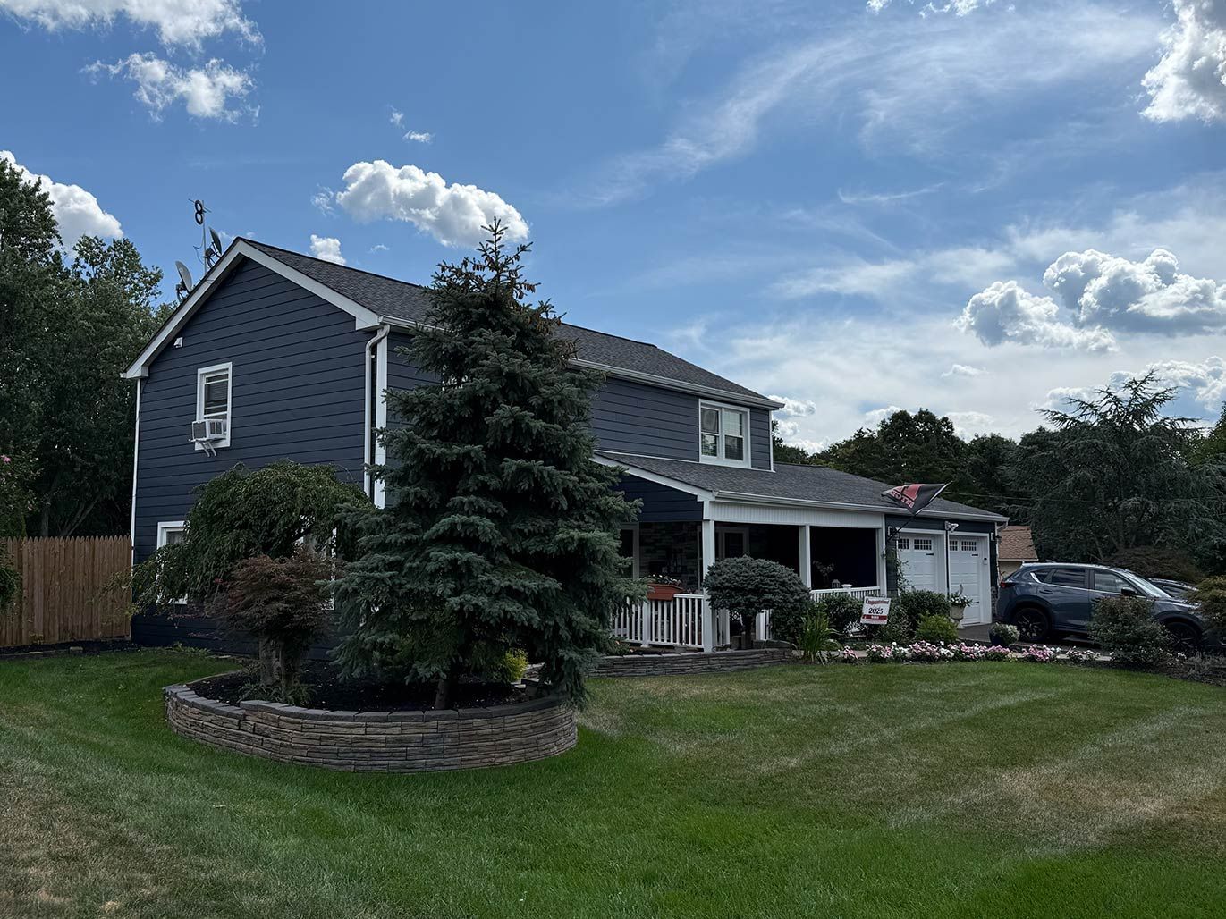 Suburban two-story house with blue siding, covered patio, and a large green lawn under a partly cloudy sky