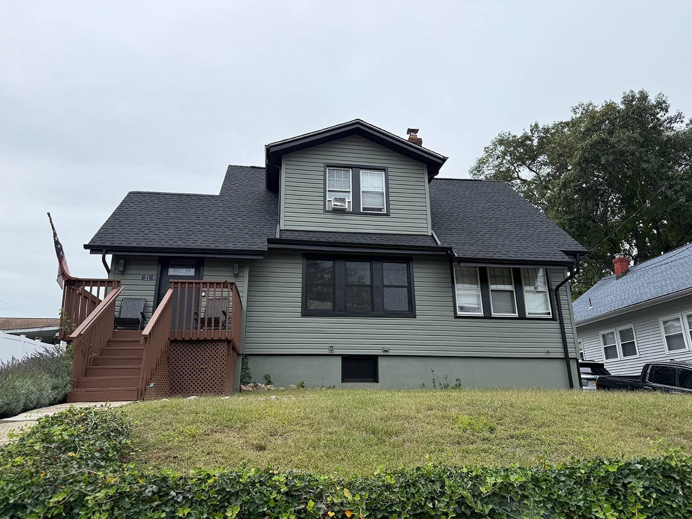 Front view of a gray house with a dark roof, wooden stairs, and a hedge in front.