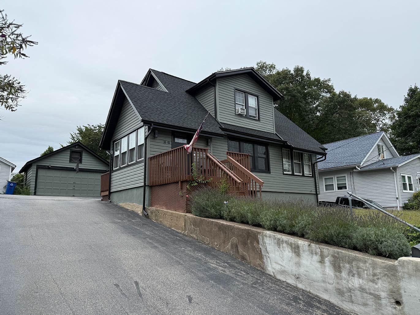 Steep gravel driveway beside a gray Victorian-style house with a gabled roof and surrounding greenery