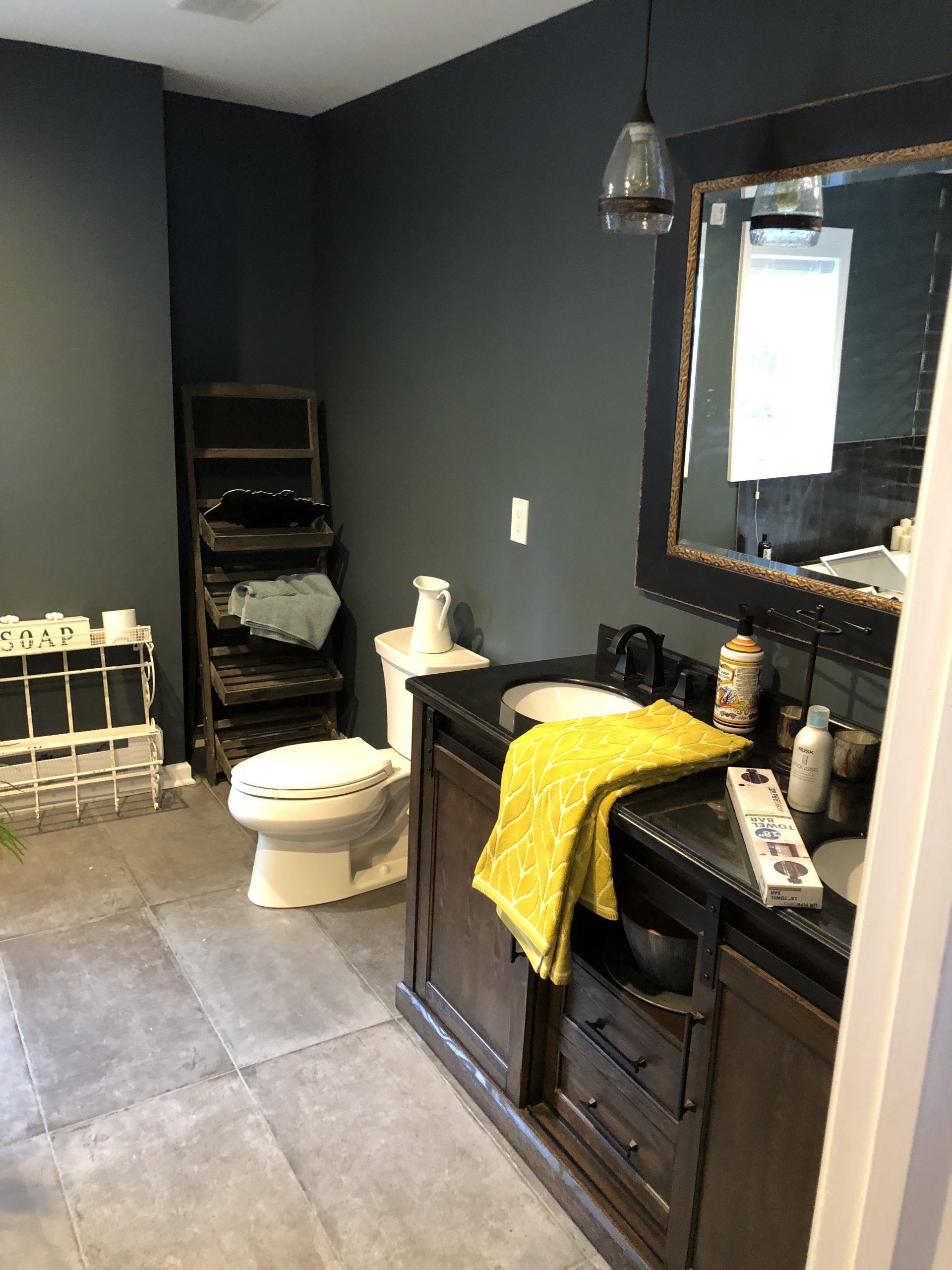 Modern black bathroom with toilet, vanity sink, large mirror, and yellow towel on counter.
