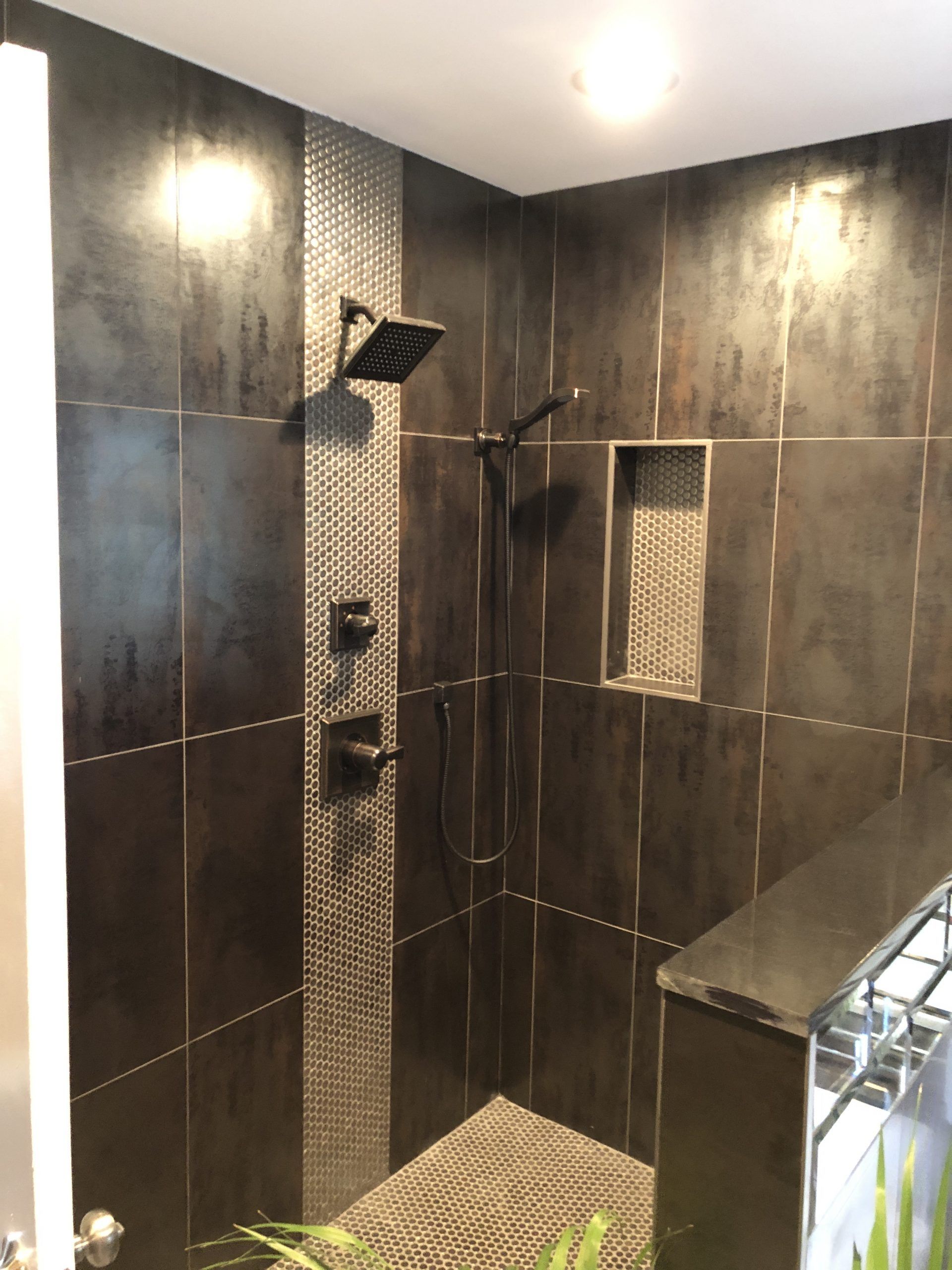 Modern tiled shower with dark walls, glass door, rain showerhead, and built-in wall shelves