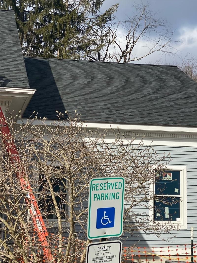 Reserved parking sign with wheelchair symbol outside a light-gray house with dark roof.