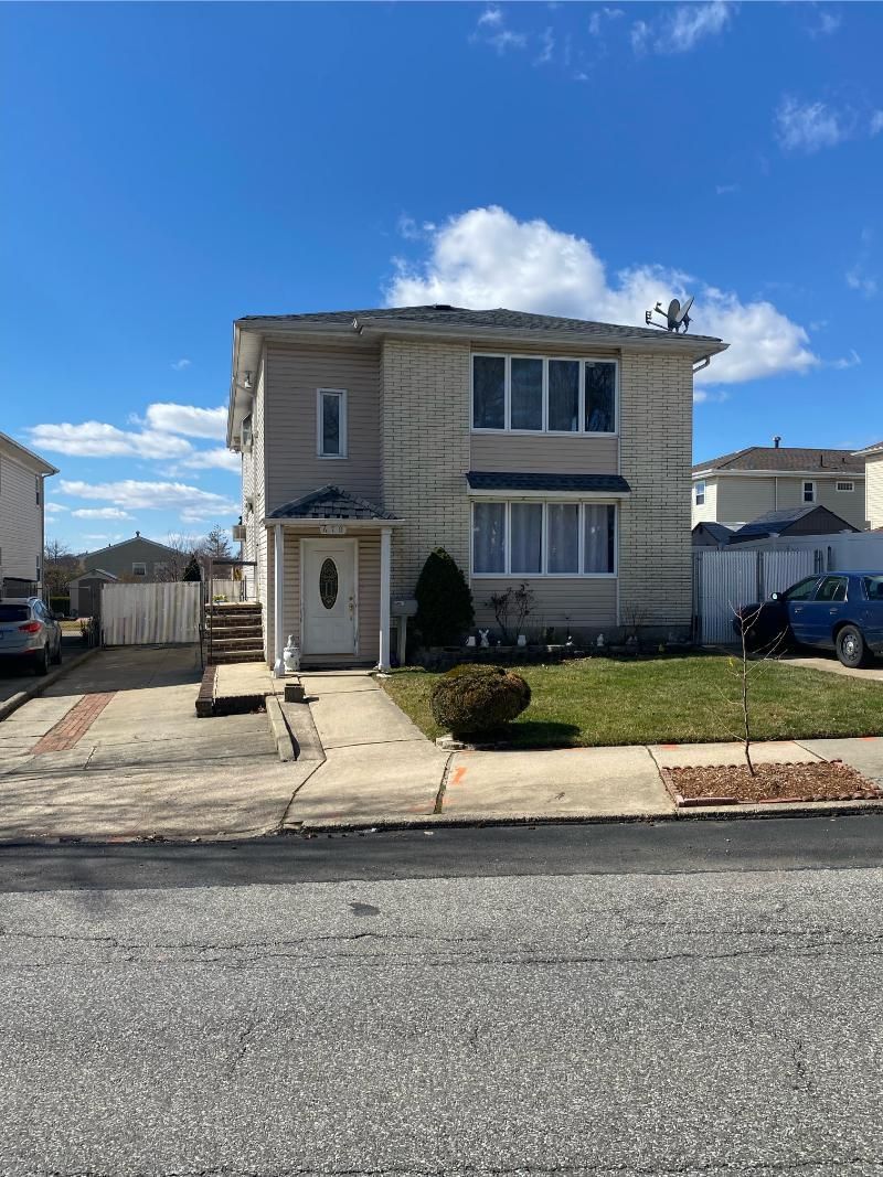 Two-story beige house with a driveway, small lawn, and blue sky on a sunny day