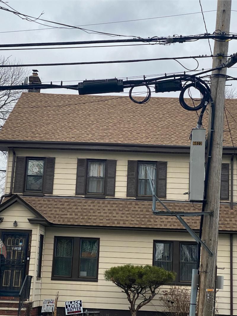 Two-story cream house with brown roof, dark shutters, and power lines crossing the front.
