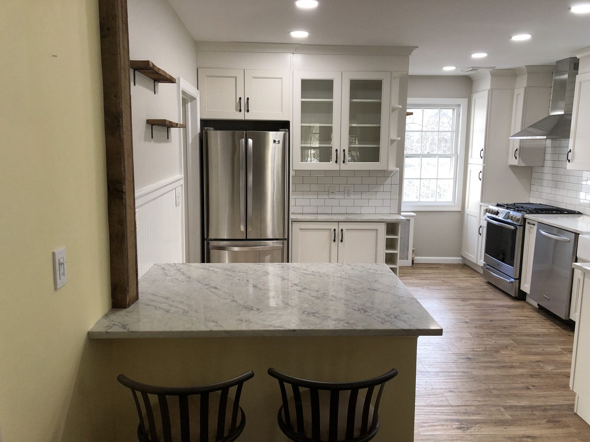 Bright white kitchen with stainless steel appliances, granite island, and two black chairs