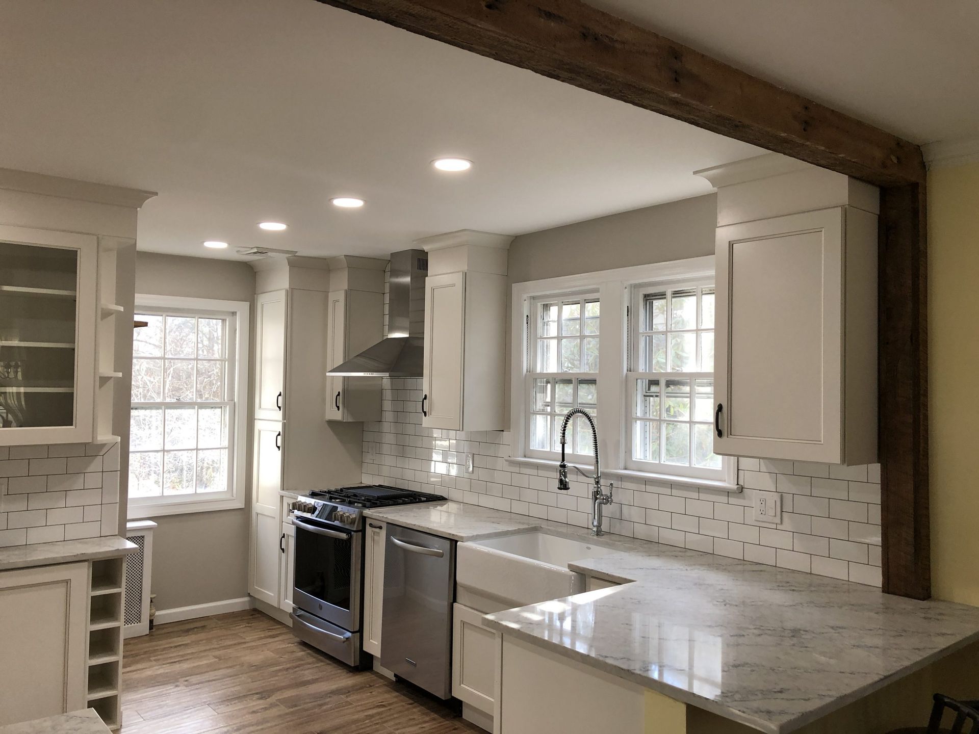 Modern white kitchen with stainless steel appliances, marble countertops, and windowed cabinets