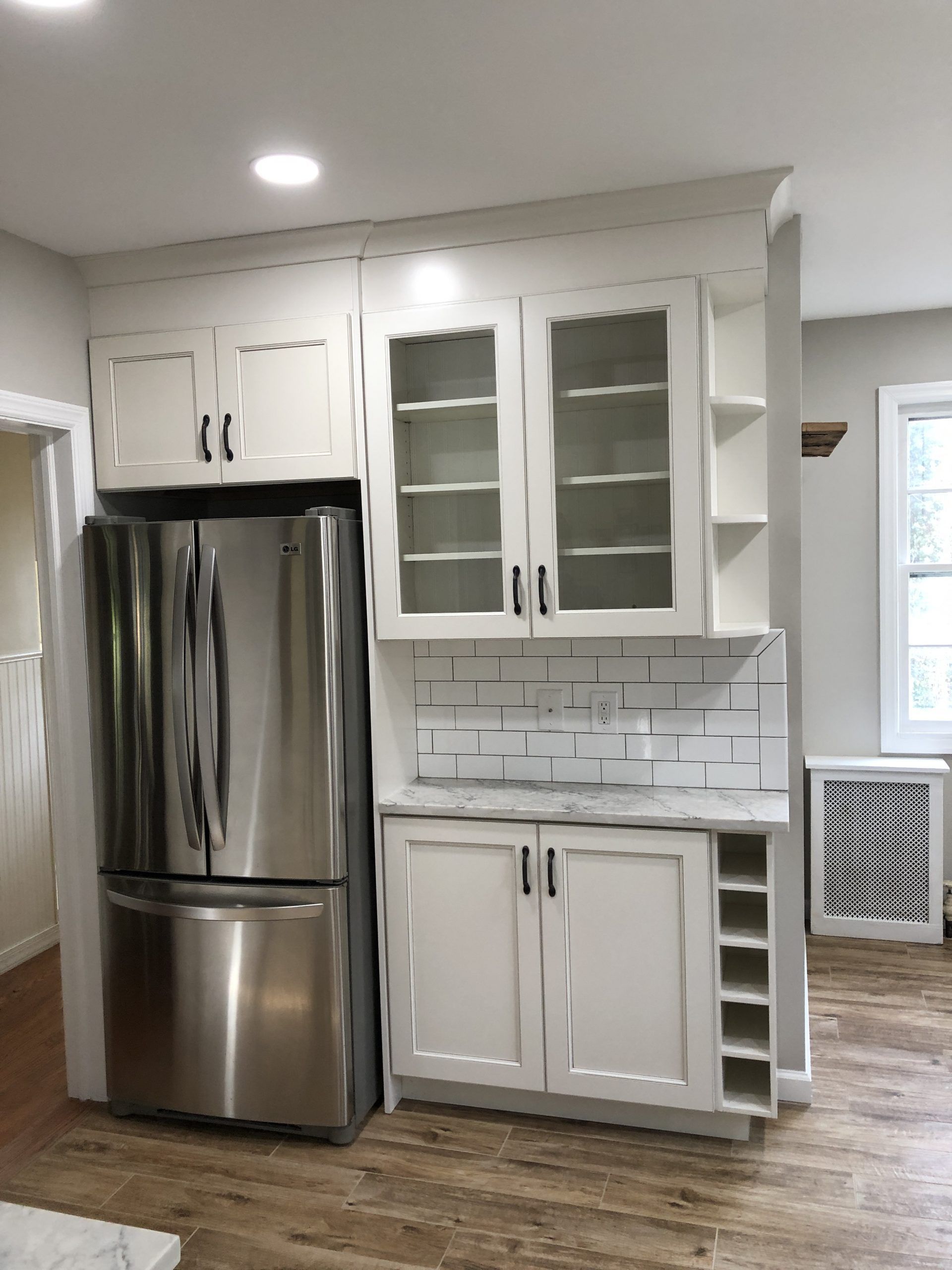 Bright kitchen with stainless steel fridge, white cabinets, subway tile backsplash, and wood-look floor