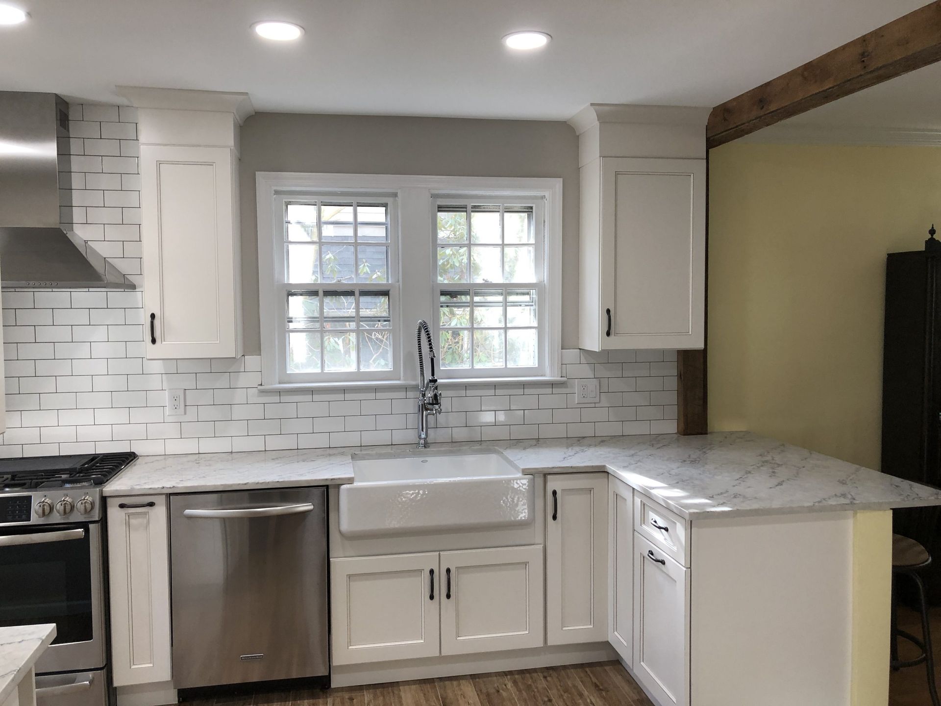 Bright white kitchen with subway tile backsplash, stainless dishwasher, and window over the sink