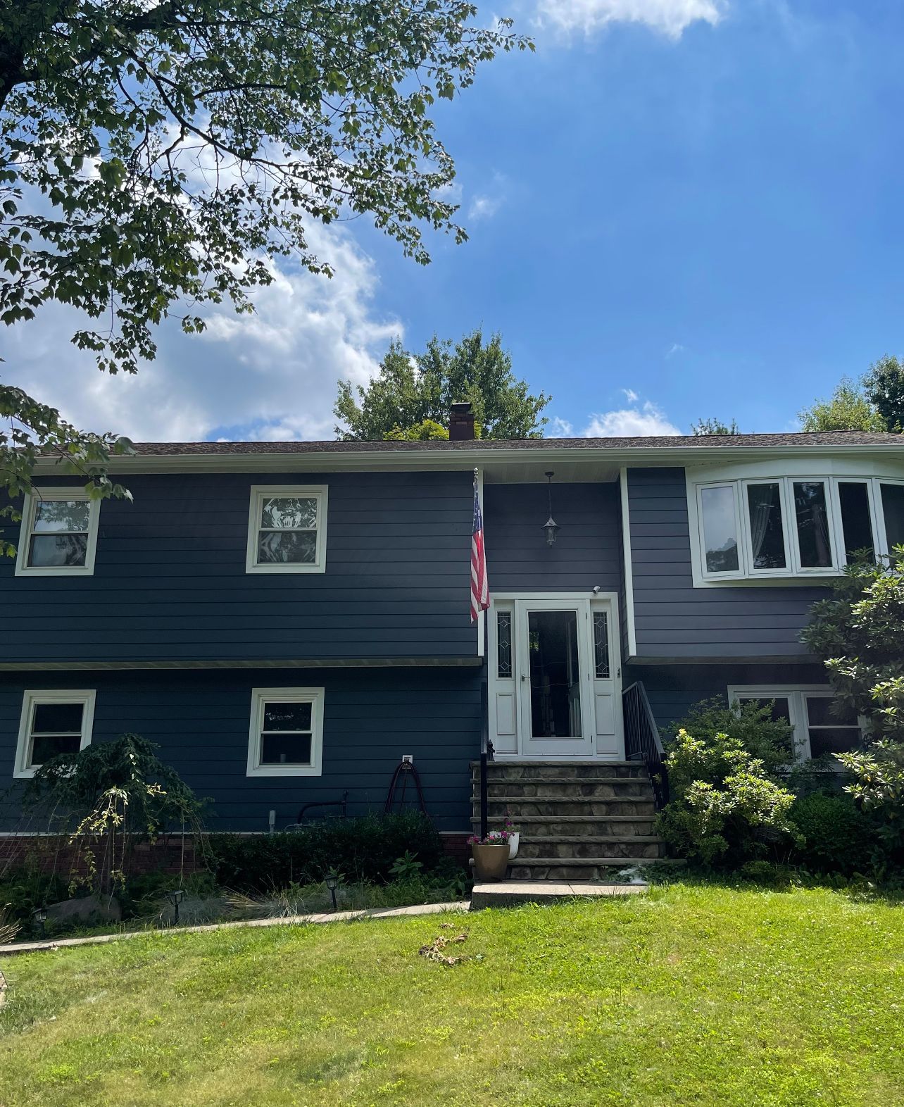 Dark blue split-level house with white trim, front steps, and an American flag under a blue sky