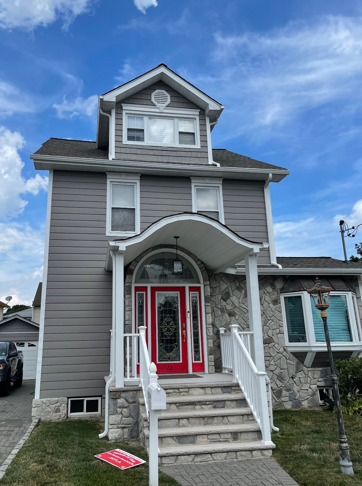 Gray two-story house with red front door and white-trimmed porch steps under a blue sky