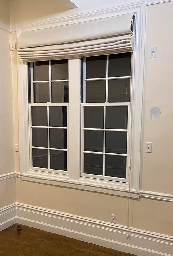 Beige room with white-trimmed double window and closed Roman shade above beige wainscoting
