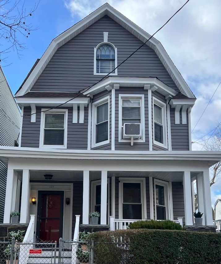 Gray Victorian house with white trim, front porch, and red front door under a blue sky