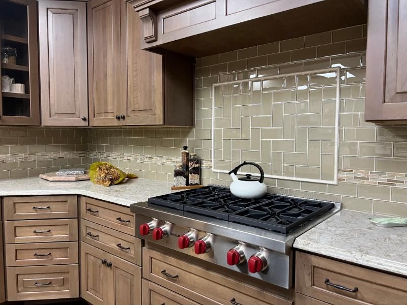 Modern kitchen with wood cabinets, tiled backsplash, and a stainless gas stove with a white kettle.