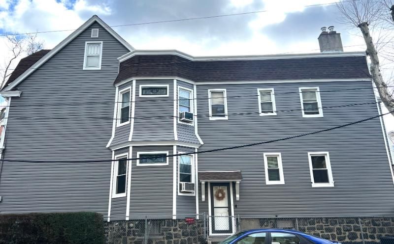 Gray two-story house with white trim and a small front bay, shot from the street under a cloudy sky