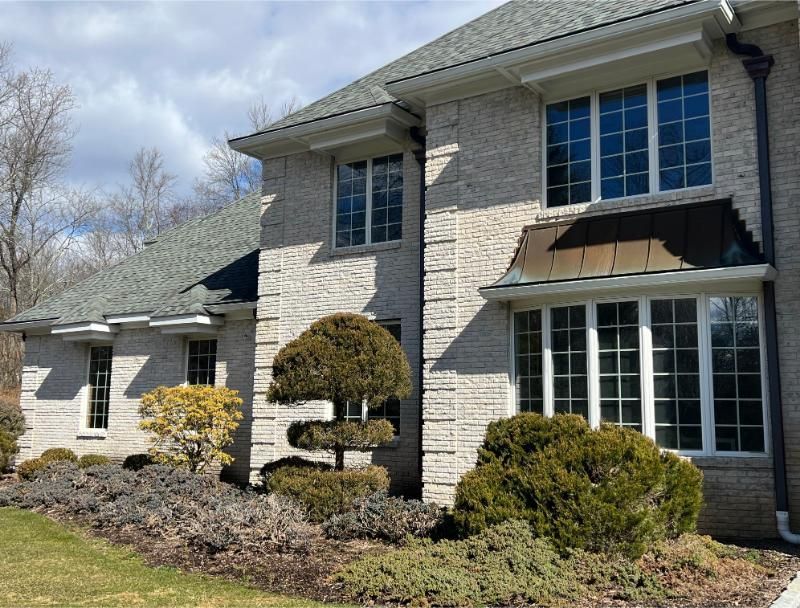 Suburban stone house with manicured shrubs and a bay window on a sunny day