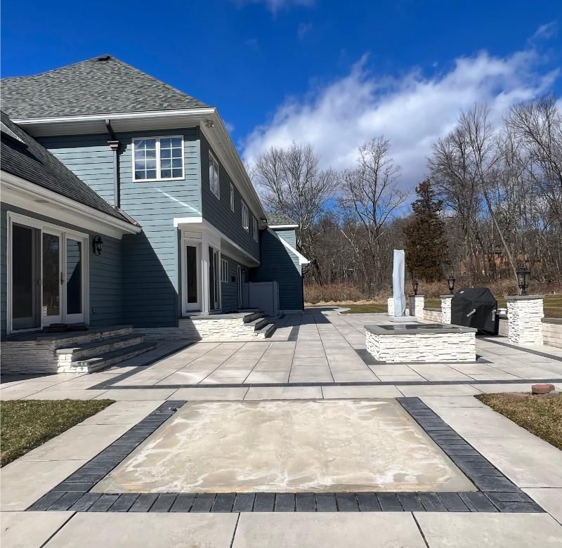 Blue house patio with stone paving, a covered porch, and a rectangular in-ground pool foundation under a clear sky