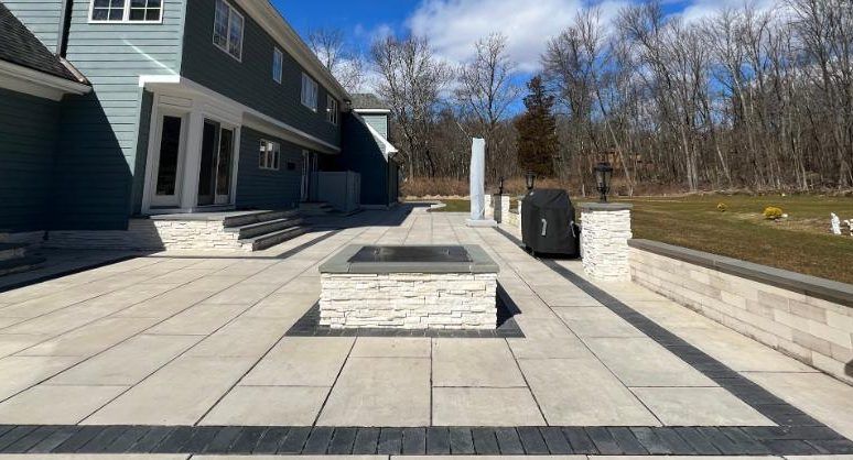 Modern backyard patio with stone pavers, raised planters, and a house in the background