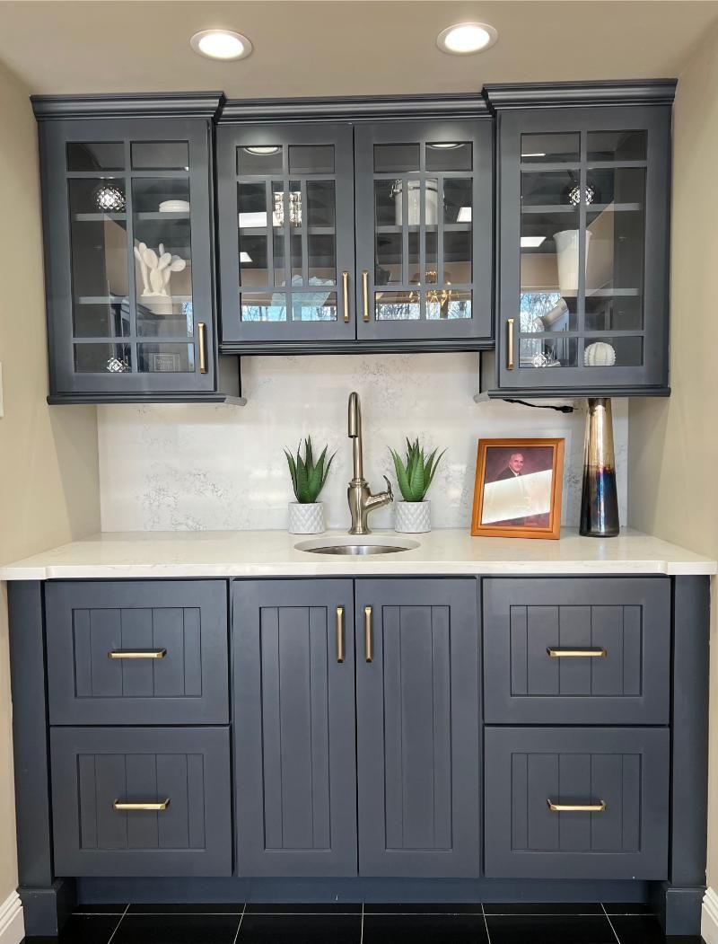 Dark gray kitchen buffet cabinet with glass-front upper cabinets, white countertop, and small decor accents.