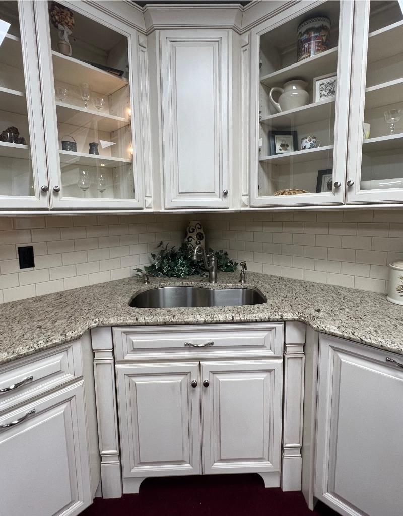 White kitchen corner with granite counters, farmhouse sink, white cabinets, and glass-front shelves with dishes