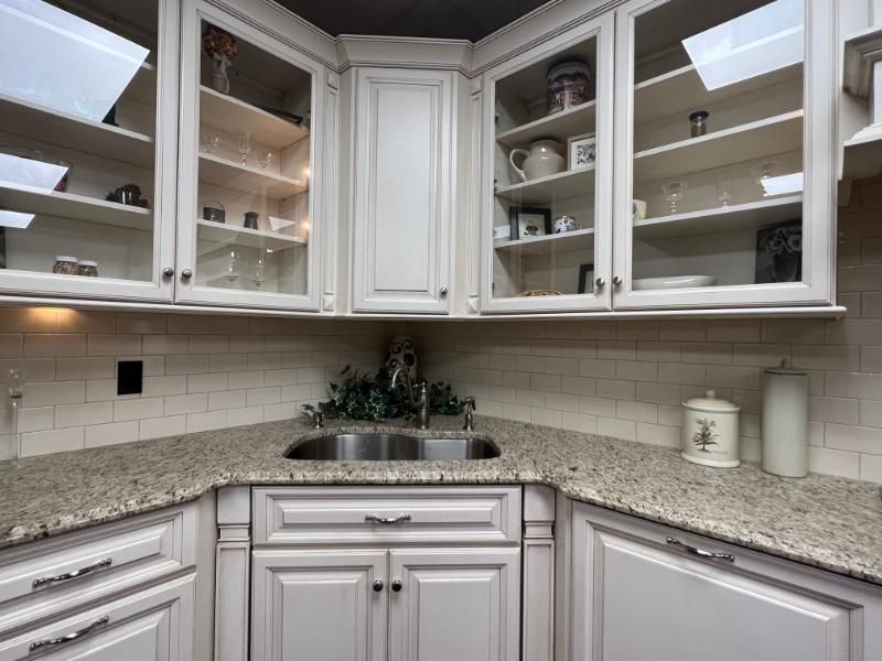 White kitchen corner with granite countertops, glass-front cabinets, and a stainless sink under under-cabinet lighting