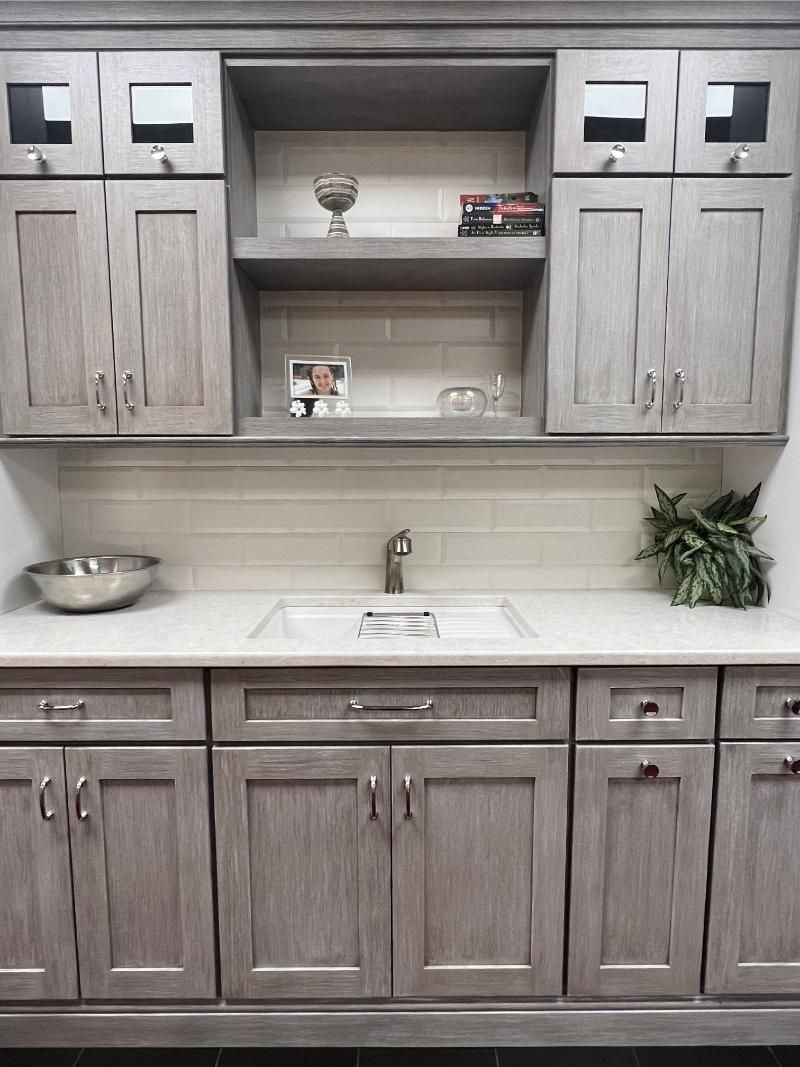 Gray kitchen cabinets, white backsplash, open shelves, and a sink centered below the counter.