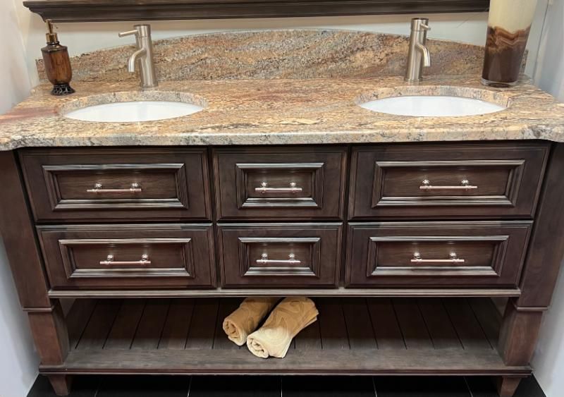 Dark wood double-sink vanity with granite countertop and two faucets under a bathroom mirror.