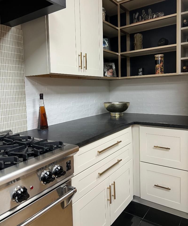 Modern kitchen corner with white cabinets, black countertops, gas stove, and open shelving