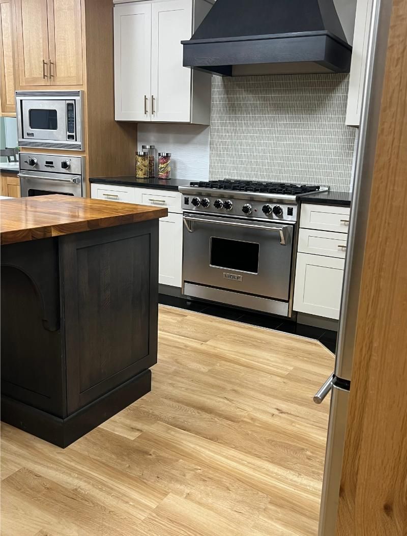 Modern kitchen with stainless steel stove, black hood, wood island, and light cabinets