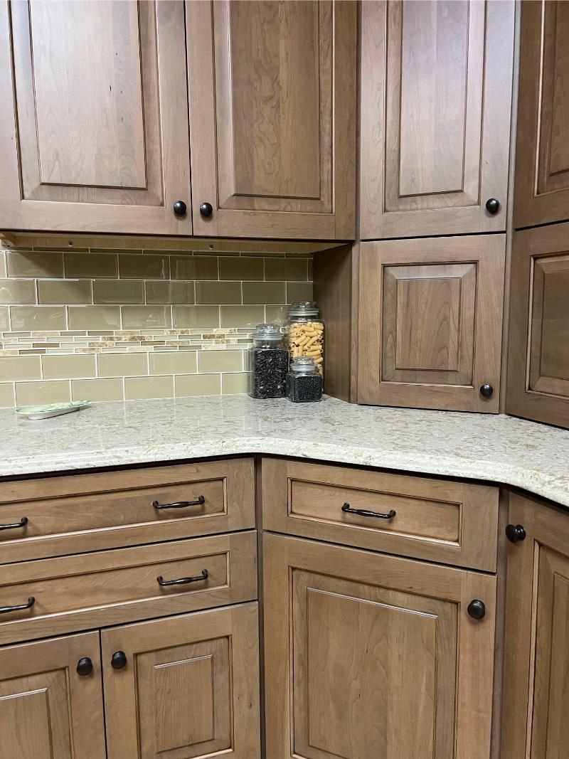 Wooden kitchen cabinets with granite countertop, light tile backsplash, and jars on the counter.