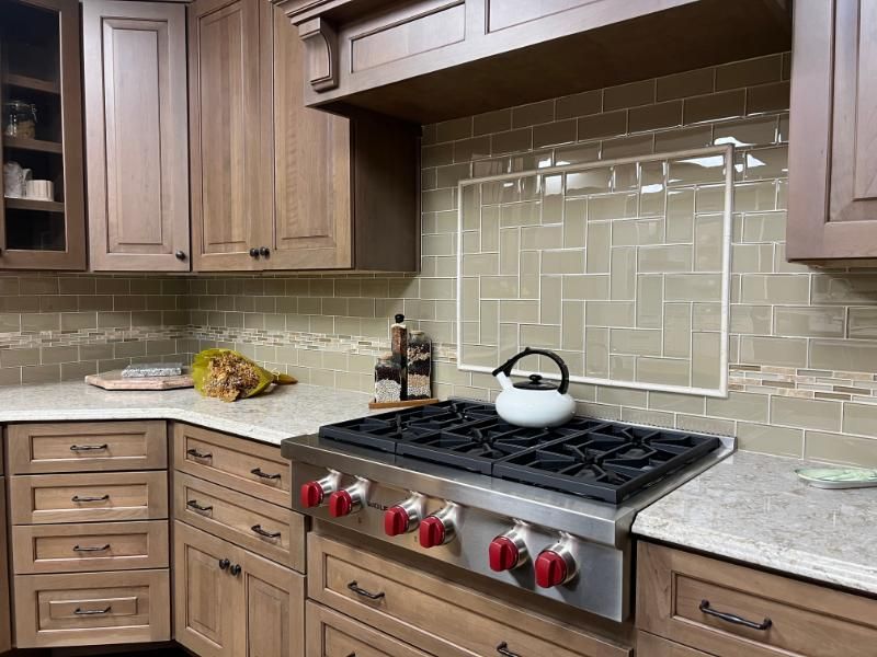 Modern kitchen with wood cabinets, beige tile backsplash, stainless range, and a white kettle on the stove.