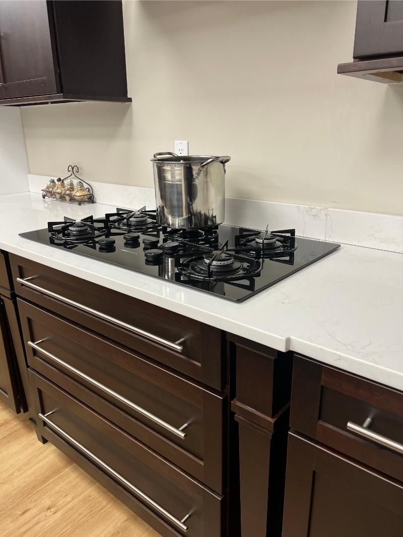 Modern kitchen countertop with a gas cooktop, stainless steel pot, and dark wood drawers