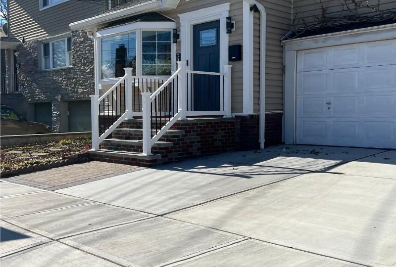 House entrance with white railings, blue front door, garage, and concrete driveway in sunlight