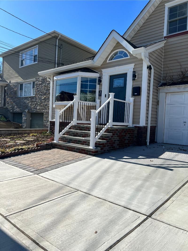 Front steps of a beige townhouse with white railings, blue front door, and driveway in bright sunlight