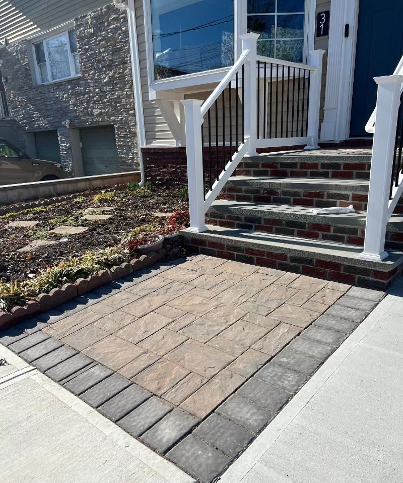 Front steps of a house with white railing, brick porch, and paved walkway leading to the entrance.