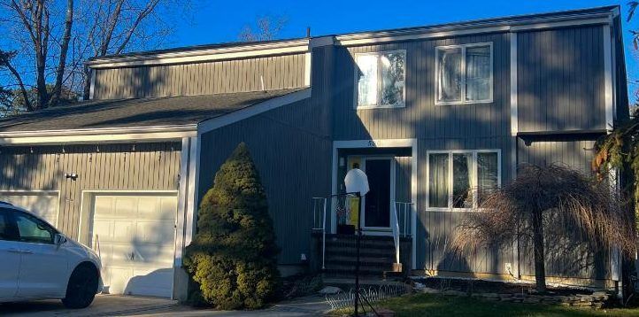 Suburban two-story house with a garage, front porch, and a parked car in sunlight