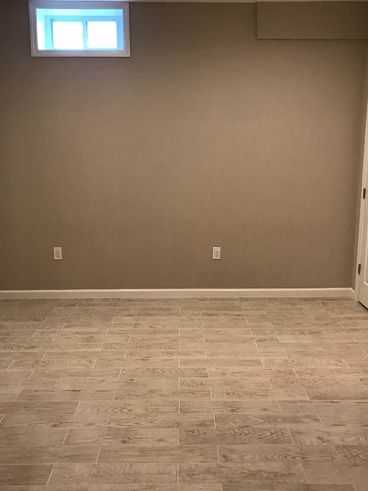 Empty room with gray walls, small high window, and light wood flooring
