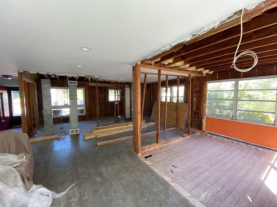Partially gutted room under renovation, with exposed framing, unfinished floor, and exposed ceiling beams