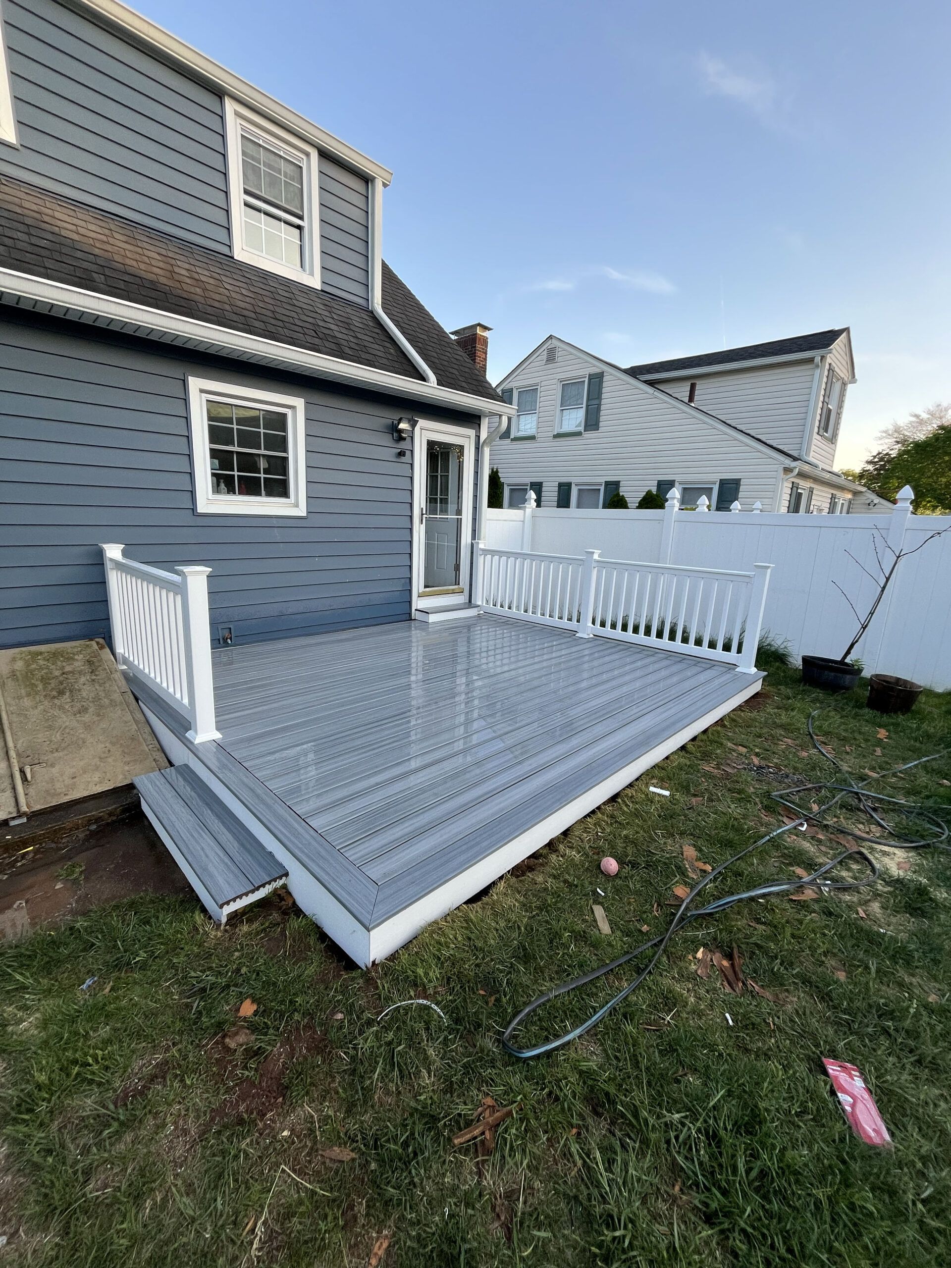 Gray house with a white wheelchair-accessible wooden ramp leading to a backyard deck.