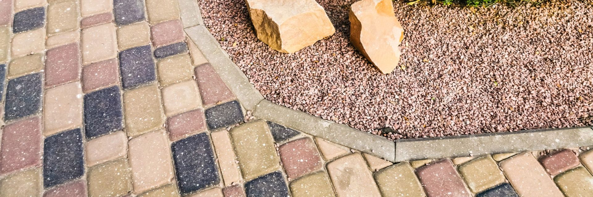 Curved mosaic walkway with beige, pink, and blue tiles beside a gravel-filled circular feature
