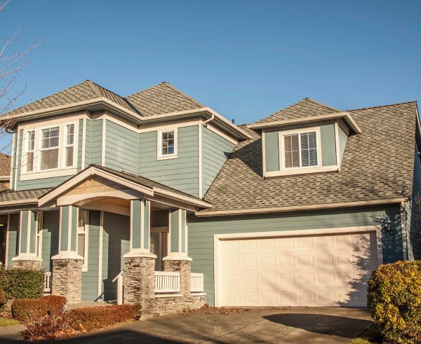 Two-story suburban house with tan siding, stone accents, and a two-car garage in daylight