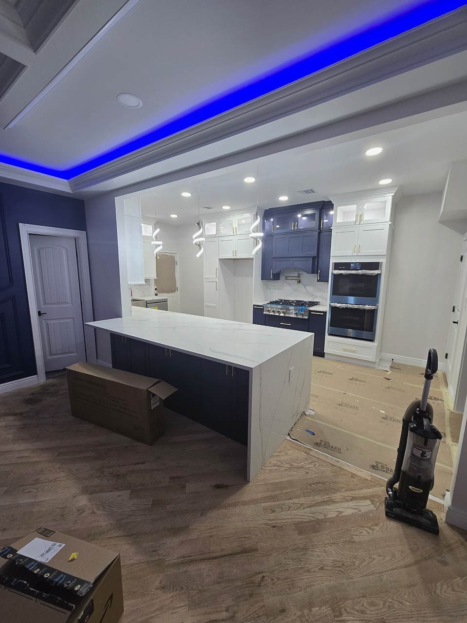 Modern kitchen with white island, dark cabinets, blue ceiling lights, and wood flooring