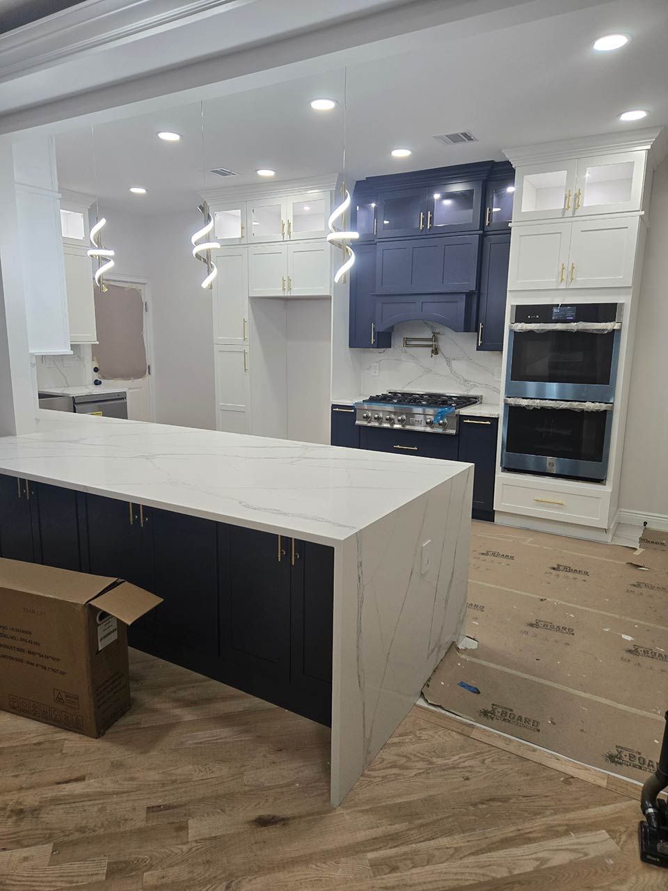 Unfinished kitchen with white cabinets, blue backsplash, large island, and cardboard on the floor