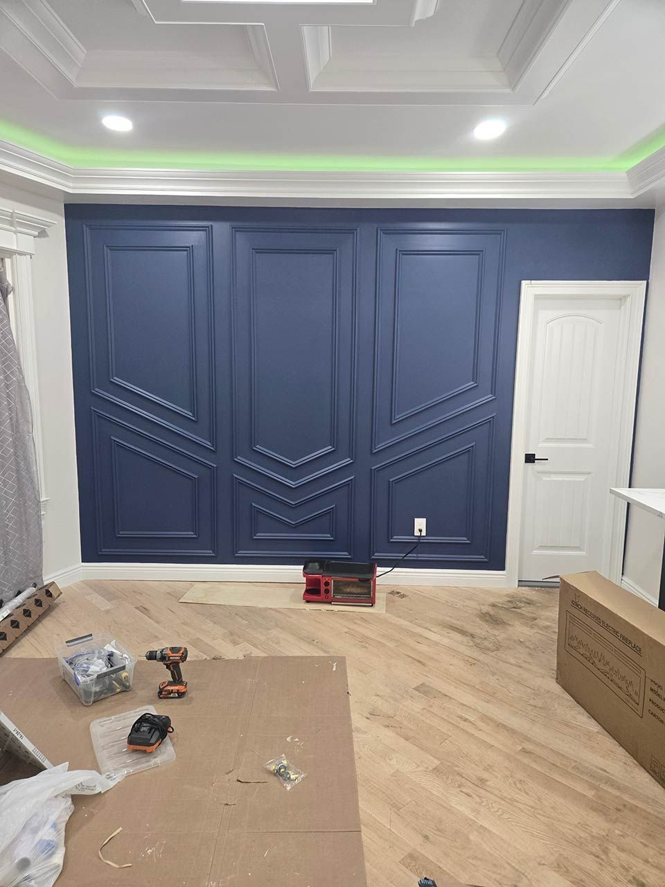 Renovated living room with navy accent wall, white door, wood floor, and tools on protective floor covering