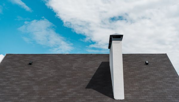 Dark shingled roof with a white chimney against a blue sky with clouds