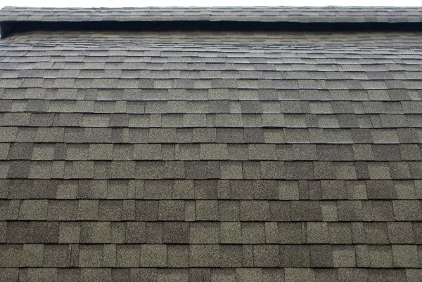 Gray shingled rooftop with a dark ridge cap and a thin strip of blue sky at the top