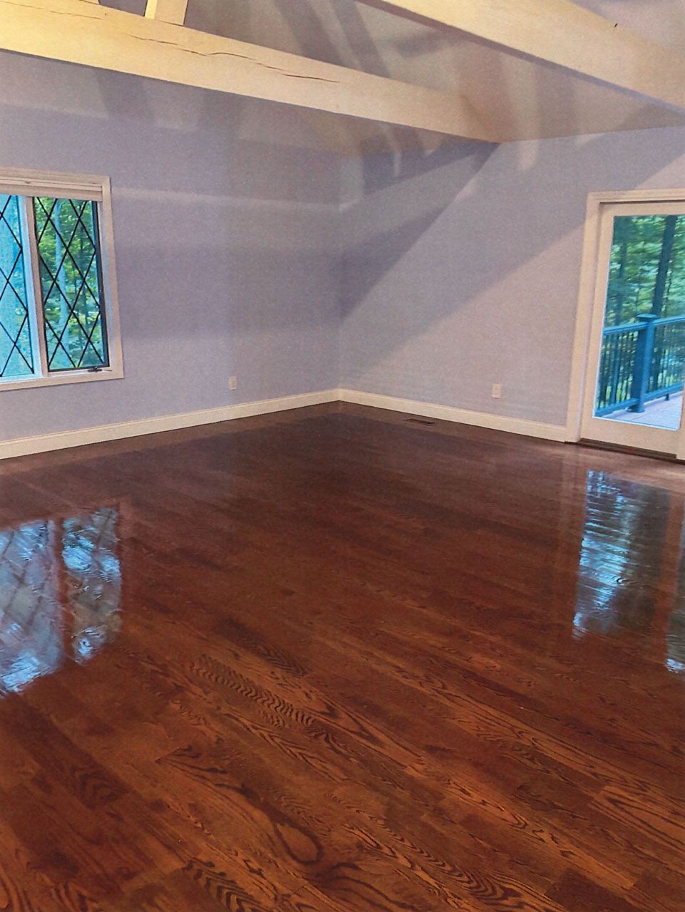 Empty room with glossy hardwood floors, gray walls, and two windows with blue curtains.