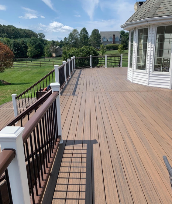 Wooden deck with black-and-white railing beside a white house, overlooking a grassy yard and trees.