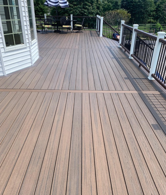 Wide wooden deck with black railings and a house siding wall overlooking trees and water